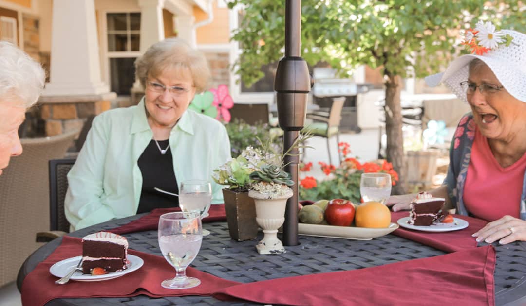 Three women sit outside eating a meal and smiling.